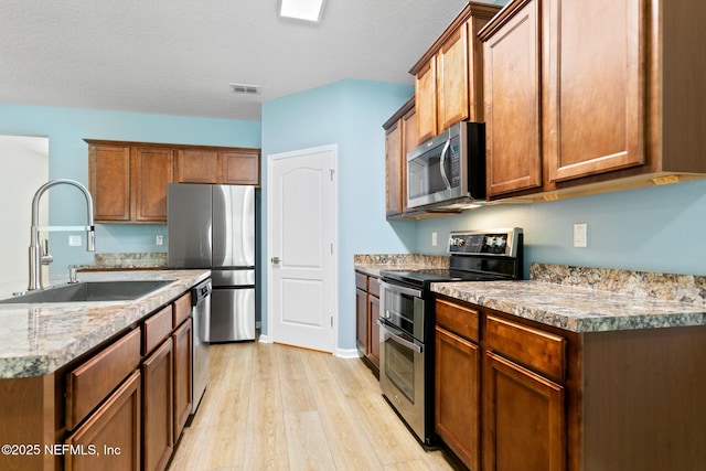 kitchen featuring stainless steel appliances, a sink, visible vents, light wood-style floors, and brown cabinets