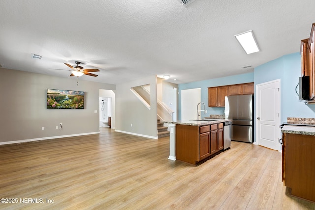 kitchen with a kitchen island with sink, stainless steel appliances, a sink, open floor plan, and brown cabinets