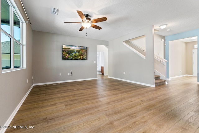 unfurnished room featuring visible vents, stairway, a ceiling fan, wood finished floors, and baseboards