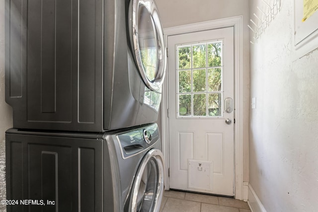 clothes washing area featuring laundry area, light tile patterned floors, baseboards, a textured wall, and stacked washing maching and dryer