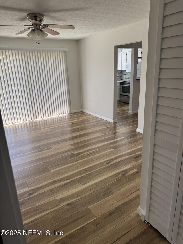 empty room with dark wood finished floors, a textured ceiling, baseboards, and ceiling fan