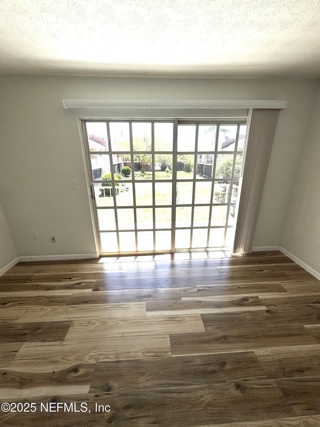 unfurnished room with a textured ceiling, wood finished floors, and a wealth of natural light