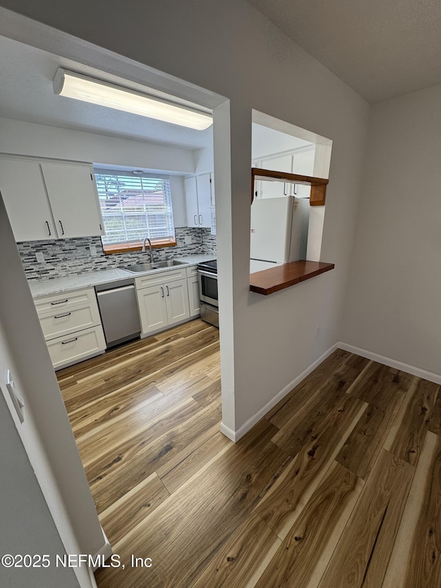 kitchen with decorative backsplash, appliances with stainless steel finishes, light wood-style floors, white cabinets, and a sink