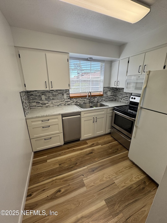 kitchen with stainless steel appliances, wood finished floors, a sink, white cabinetry, and decorative backsplash