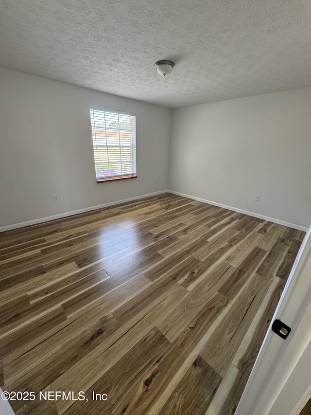 unfurnished room with dark wood-style flooring, a textured ceiling, and baseboards