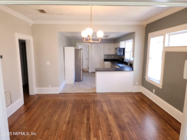 kitchen with dark countertops, ornamental molding, wood finished floors, a peninsula, and an inviting chandelier