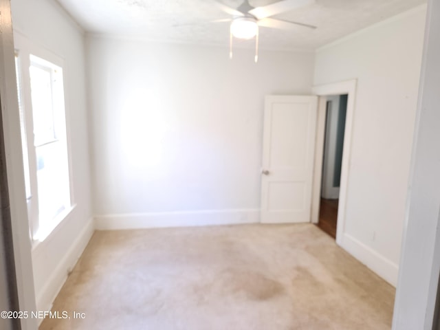 spare room with a ceiling fan, light colored carpet, and baseboards