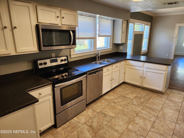 kitchen with crown molding, visible vents, appliances with stainless steel finishes, a sink, and a peninsula