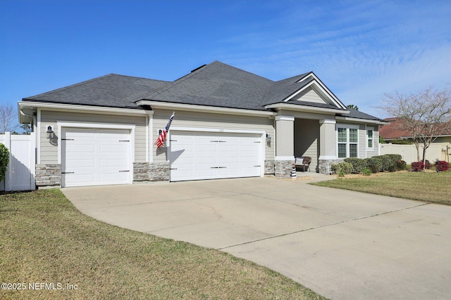 view of front of house featuring an attached garage, concrete driveway, stone siding, roof with shingles, and a front lawn