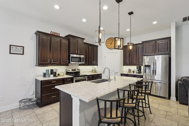 kitchen with dark brown cabinetry, an island with sink, appliances with stainless steel finishes, a kitchen bar, and a sink