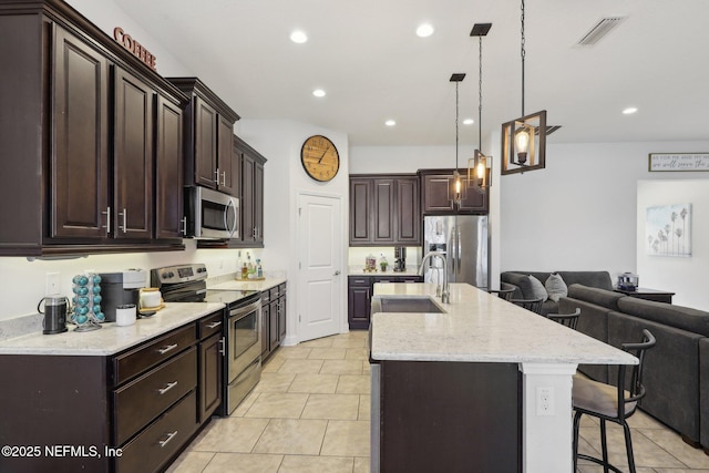 kitchen featuring a breakfast bar area, stainless steel appliances, visible vents, open floor plan, and a sink