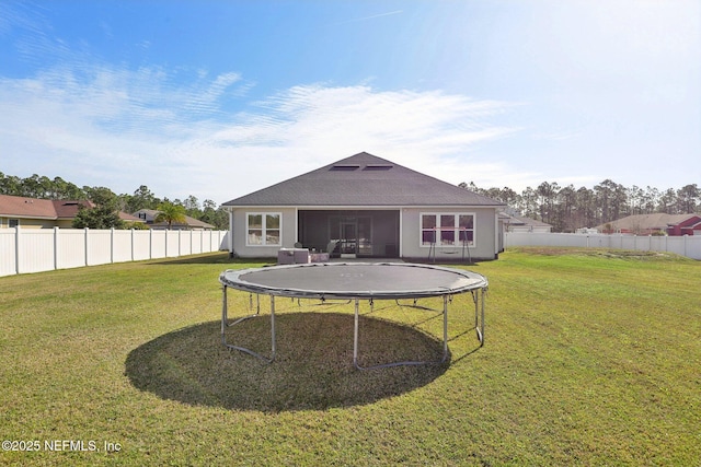 back of house featuring a trampoline, a fenced backyard, and a yard