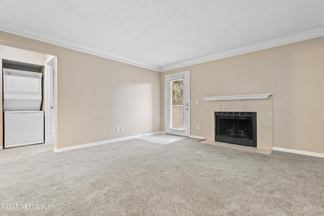 unfurnished living room with a tiled fireplace, ornamental molding, stacked washer / drying machine, a textured ceiling, and carpet flooring