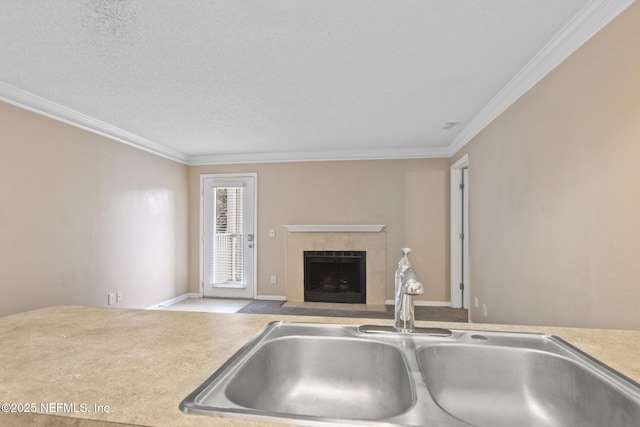 kitchen with light countertops, a tiled fireplace, ornamental molding, a sink, and a textured ceiling