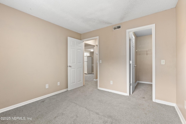 unfurnished bedroom with baseboards, visible vents, a walk in closet, and carpet flooring