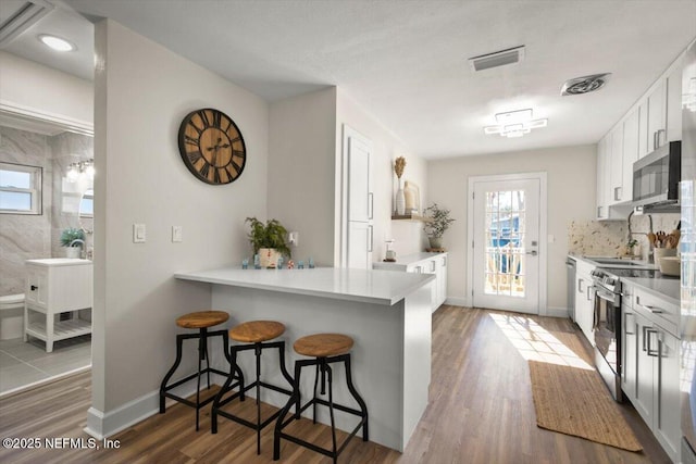 kitchen featuring stainless steel appliances, a breakfast bar, wood finished floors, white cabinets, and light countertops