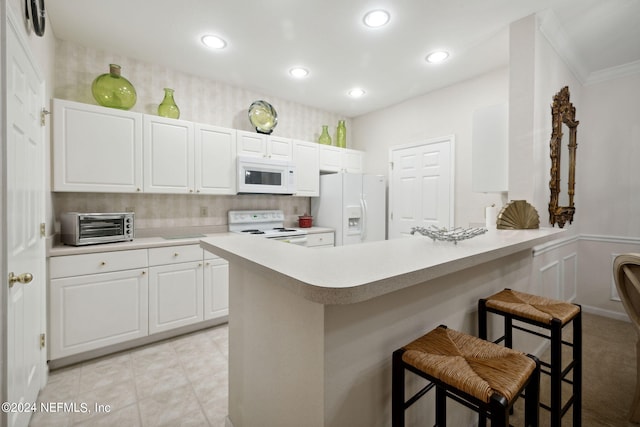 kitchen featuring a toaster, white cabinetry, white appliances, a peninsula, and a kitchen breakfast bar