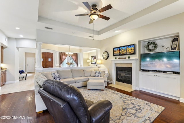 living area with ceiling fan with notable chandelier, a raised ceiling, decorative columns, and wood finished floors