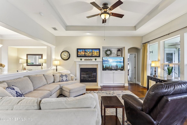 living room with dark wood finished floors, visible vents, ceiling fan, and a tray ceiling