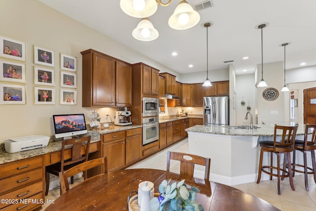 kitchen with visible vents, a sink, stainless steel appliances, under cabinet range hood, and a kitchen breakfast bar