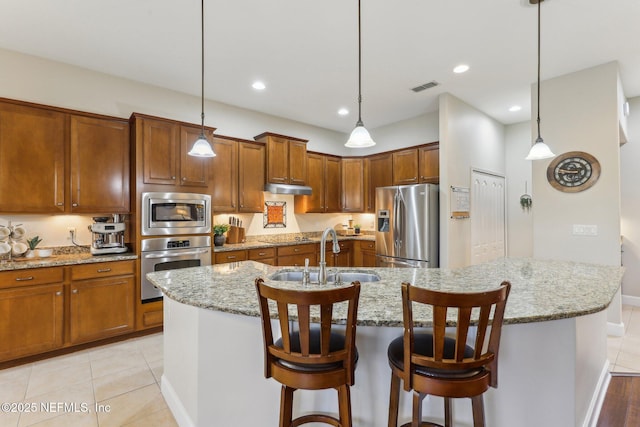 kitchen featuring a center island with sink, visible vents, a sink, under cabinet range hood, and appliances with stainless steel finishes