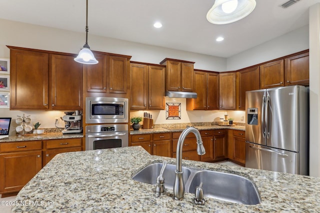 kitchen with light stone counters, a sink, hanging light fixtures, under cabinet range hood, and appliances with stainless steel finishes