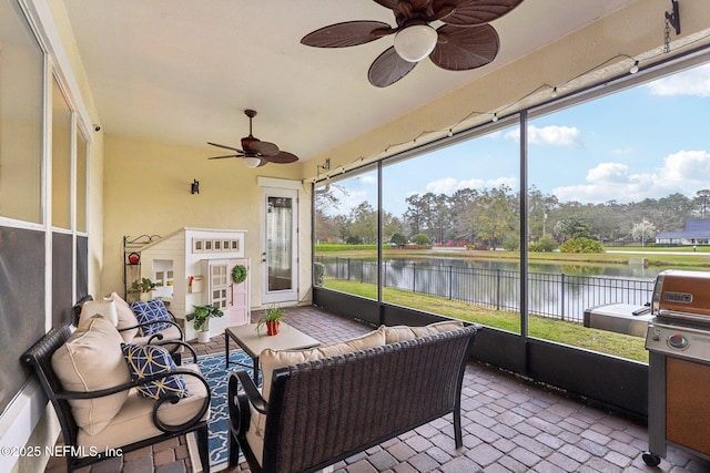 sunroom with a ceiling fan and a water view