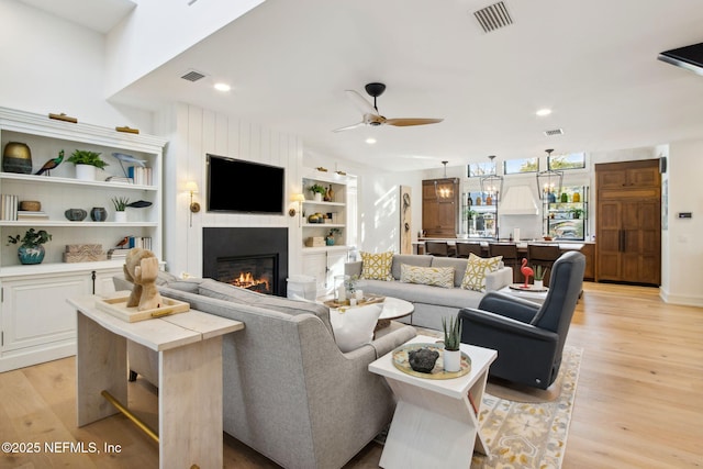 living area with light wood-type flooring, a glass covered fireplace, and visible vents