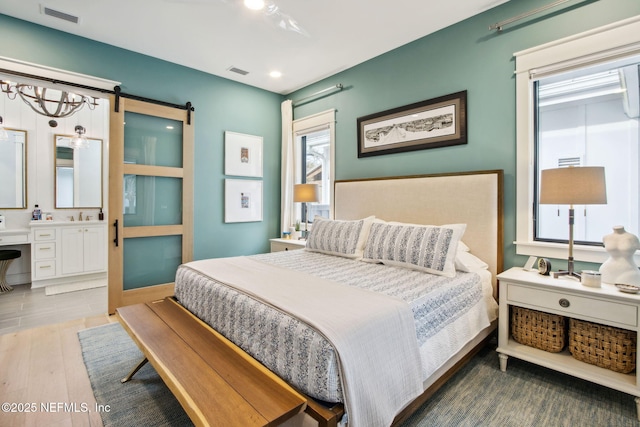 bedroom featuring a barn door, ensuite bath, wood finished floors, and visible vents