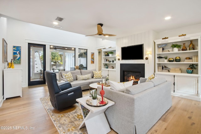 living room with light wood finished floors, a fireplace, visible vents, and a ceiling fan