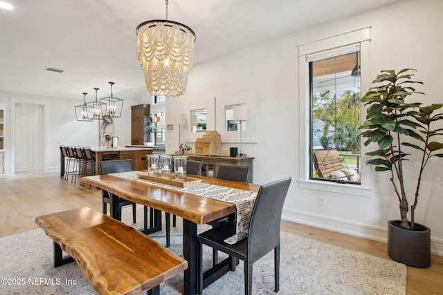 dining area featuring light wood-style floors, visible vents, baseboards, and a notable chandelier