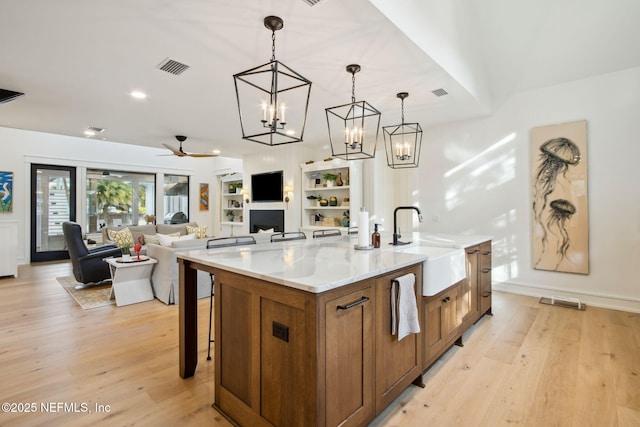 kitchen with brown cabinets, visible vents, a kitchen island with sink, a sink, and light wood-type flooring