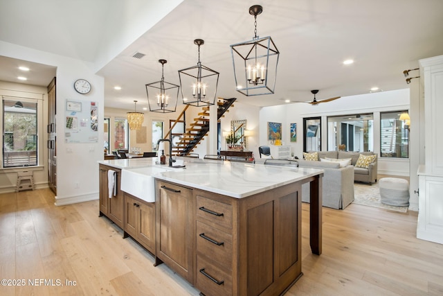 kitchen with a center island with sink, a sink, light wood-style flooring, and pendant lighting