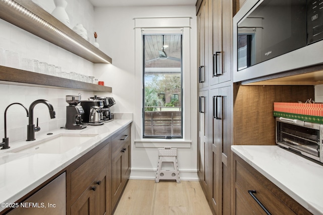 kitchen featuring a toaster, a sink, light wood-style floors, open shelves, and tasteful backsplash