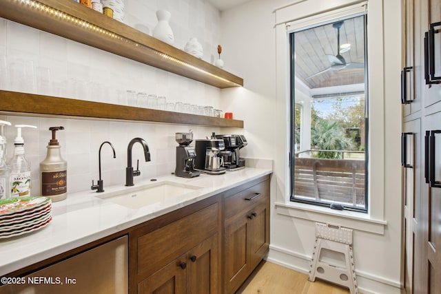 bar featuring light wood-style floors, baseboards, decorative backsplash, and a sink