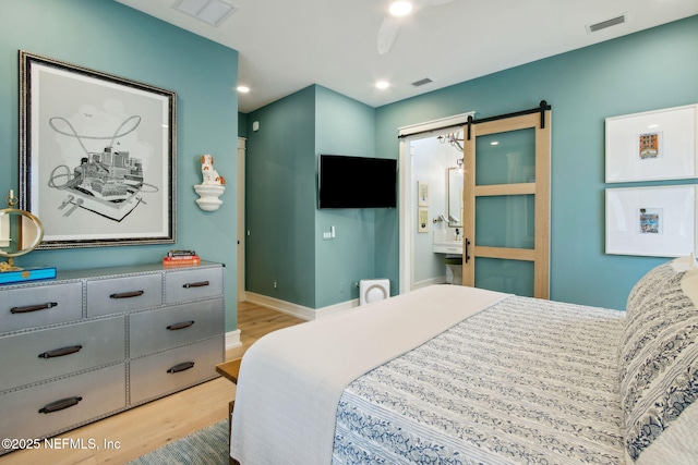 bedroom with a barn door, visible vents, baseboards, connected bathroom, and light wood-type flooring