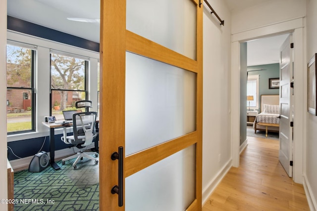 hall with a barn door, baseboards, and wood finished floors