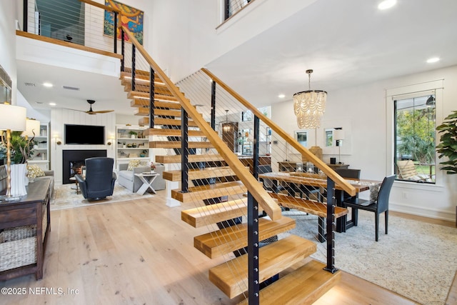 staircase featuring a chandelier, recessed lighting, a fireplace, wood finished floors, and a towering ceiling