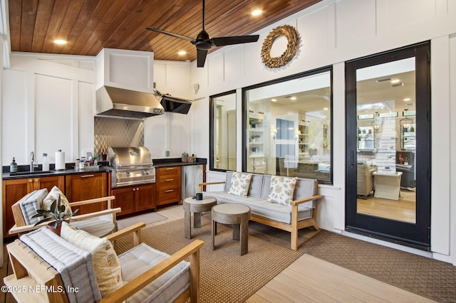 kitchen with wooden ceiling, a decorative wall, a sink, light wood-type flooring, and wall chimney exhaust hood