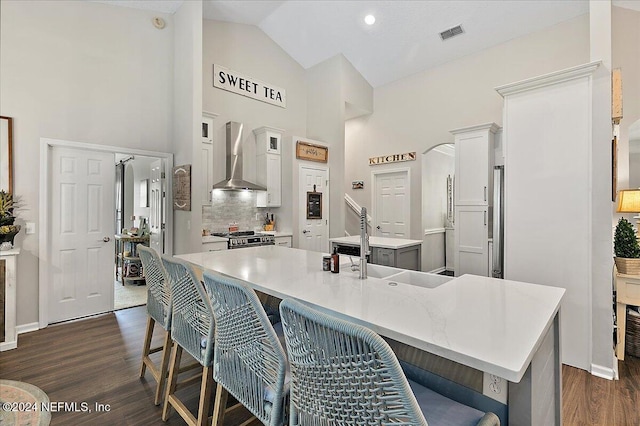 kitchen with a breakfast bar area, stainless steel appliances, a sink, wall chimney exhaust hood, and a center island with sink