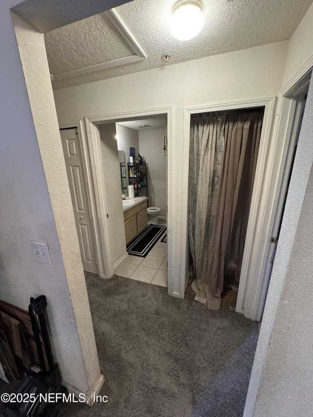 hallway featuring light colored carpet, a textured ceiling, and light tile patterned floors