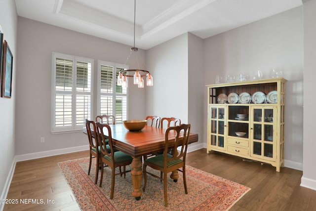 dining room with a raised ceiling, a notable chandelier, ornamental molding, wood finished floors, and baseboards