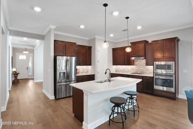 kitchen featuring a center island with sink, light wood finished floors, a sink, light countertops, and appliances with stainless steel finishes