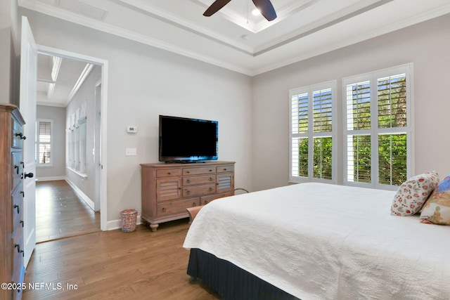 bedroom featuring ornamental molding, a tray ceiling, wood finished floors, baseboards, and ceiling fan