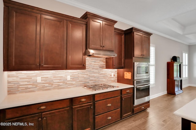 kitchen with under cabinet range hood, backsplash, stainless steel appliances, crown molding, and light countertops