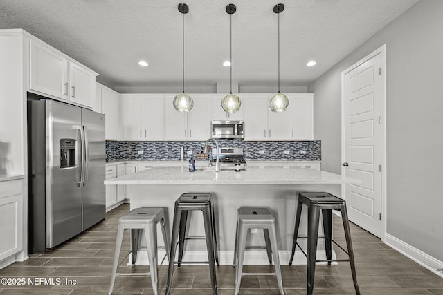 kitchen with appliances with stainless steel finishes, wood finish floors, white cabinets, and backsplash