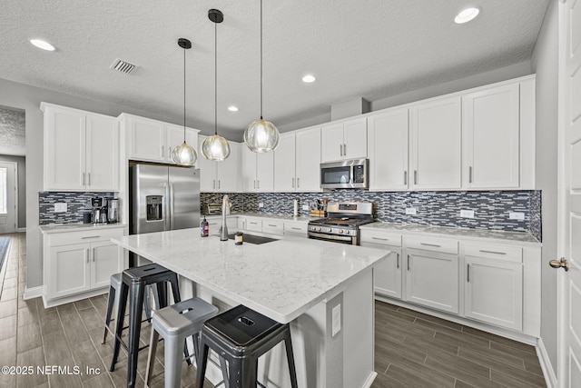 kitchen featuring a center island with sink, visible vents, appliances with stainless steel finishes, wood tiled floor, and a sink