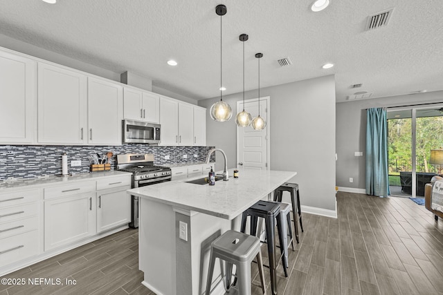 kitchen with stainless steel appliances, wood finish floors, a sink, visible vents, and tasteful backsplash