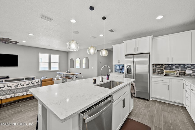 kitchen featuring a sink, open floor plan, appliances with stainless steel finishes, backsplash, and a center island with sink