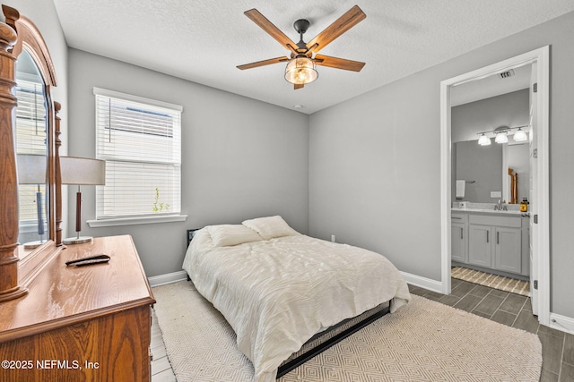 bedroom with a textured ceiling, connected bathroom, a sink, visible vents, and baseboards